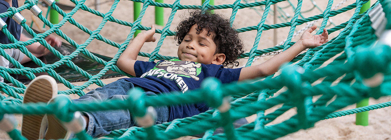 Ein Kind liegt in einem grünen Kletternetz auf einem Spielplatz in den Gärten der Welt