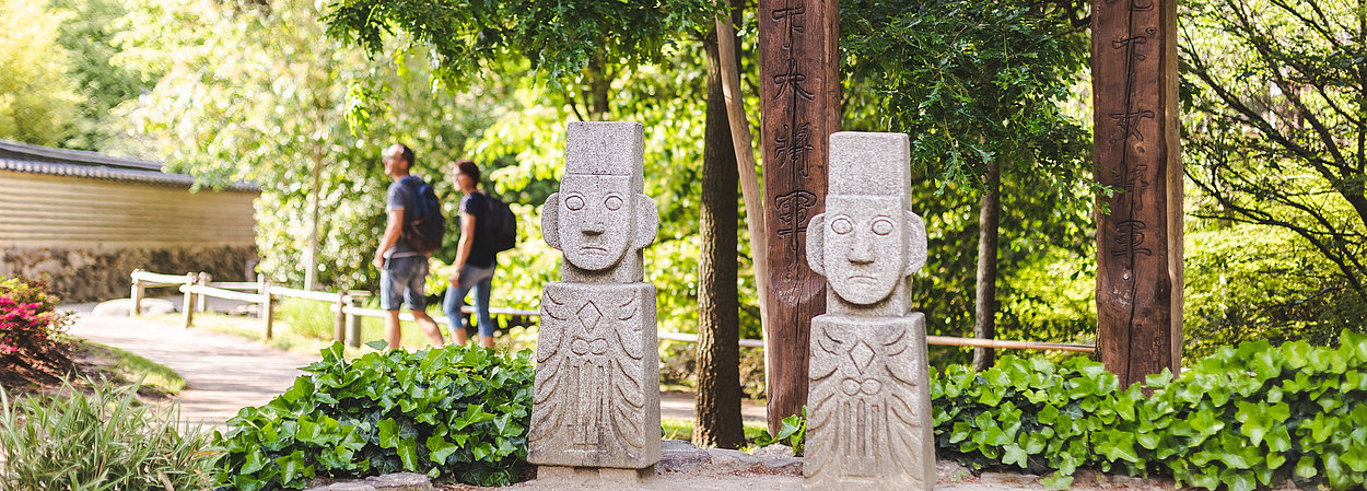 Zwei Statuen im Koreanischen Garten, im Hintergrund Menschen