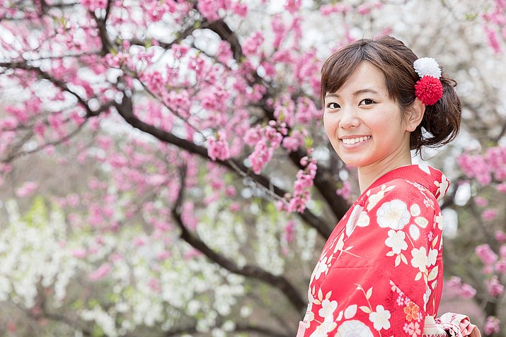 Frau in Kimono steht vor Baum mit Kirschblüten