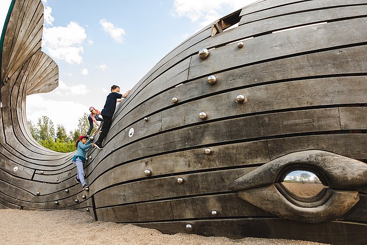 Kinder klettern einen Wal aus Holz auf einem Spielplatz in den Gärten der Welt hoch