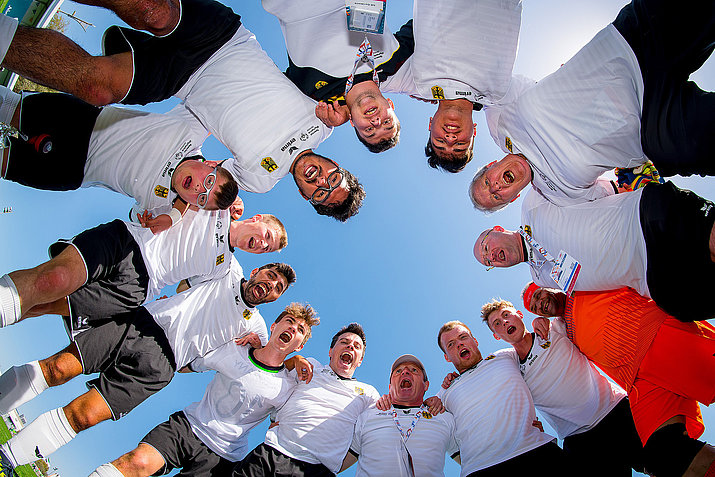 Aufnahme einer im Kreis zusammenstehenden Sportmannschaft von unten, oben blauer Himmel